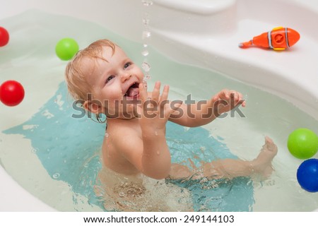 Funny little baby girl in the bath  playing with water drops and splashes