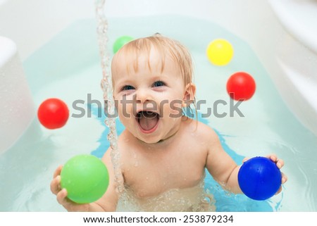 Funny little baby girl in the bath playing with water drops and splashes