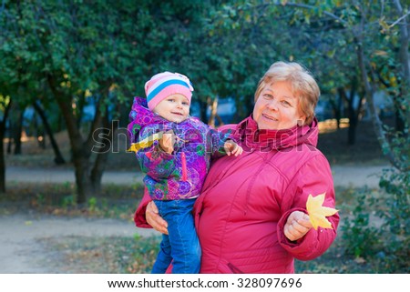 Happy senior lady and a little toddler girl, grandmother and granddaughter, enjoying a walk in the park. Child and  grandparent. autumns day. Grandmother and little girl happy together in the garden