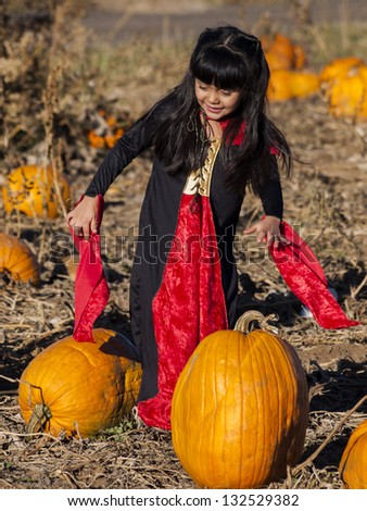 Young family with kids in costumes looking for big pumpkin on pumpkin patch.