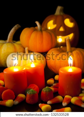 Lit orange candles with small pumpkins and jack-o\'-lantern on black background.