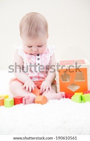 Baby girl playing with her toys on a white blanket.