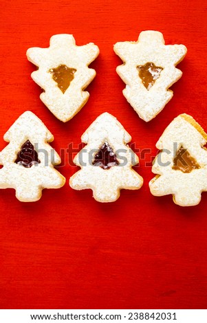 Linzer cookies in shape of Christmas tree on red background.