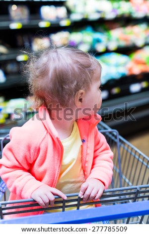 Cute toddler girl sitting in shopping cart at the grocery store.