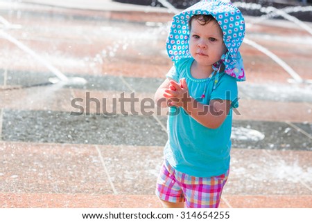 Cute toddler girl playing with small fountains in splash park.