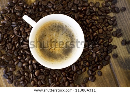 Cup of coffee and coffee seeds on wooden table top view.