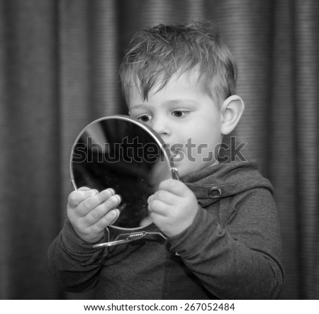 little boy looking at himself in a hand mirror in black and white