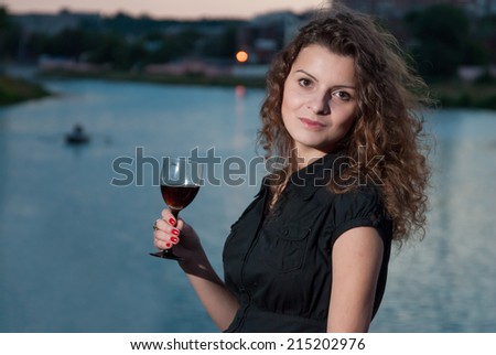 Cheerful young girl drinking wine from glass near river