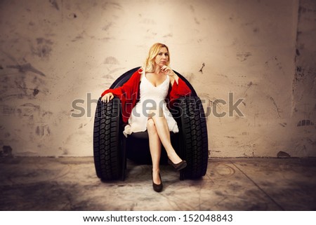 White girl in a white dress and red scarf on a chair made of tires in a grunge environment