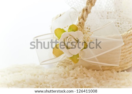 Close up to the rice for wedding accompanied by a basket decorated with a flower on a white background.