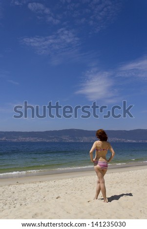 Photograph of a beautiful woman in bikini on the beach watching the sea.