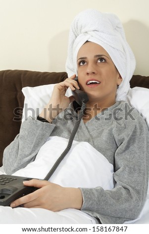 Young woman talking on phone in bed with a towel on her head.