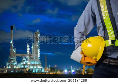 Engineer holding a yellow helmet for the safety of workers on the background oil refinery. Beautiful sky at dawn