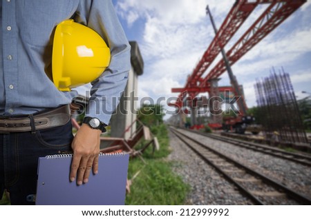 Engineer holding yellow helmet for workers security on background of construction cranes.