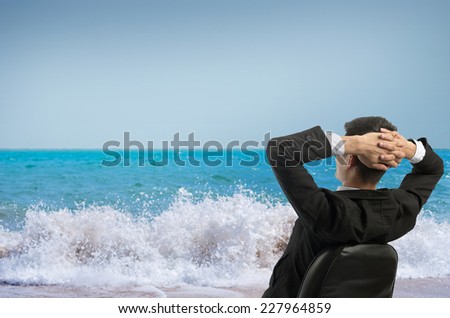 Young businessman sitting on a chair in front of the sea and looking up at the sky. Vacation work