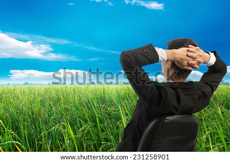 Young businessman sitting on a chair in front of a field of grass and look up at the sky. Vacation work
