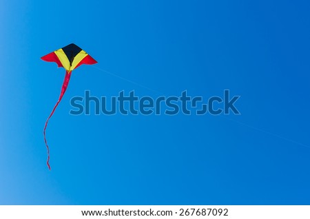 Kite triangular, yellow, red, black, flying high in the clear blue sky.