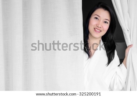 Asian woman smiling wearing a white robe, opened the curtains in the room.
