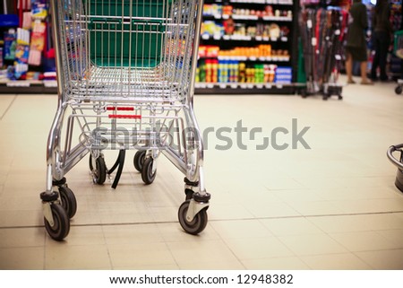 Empty shopping cart in big store with products and few people in background. Shop concept