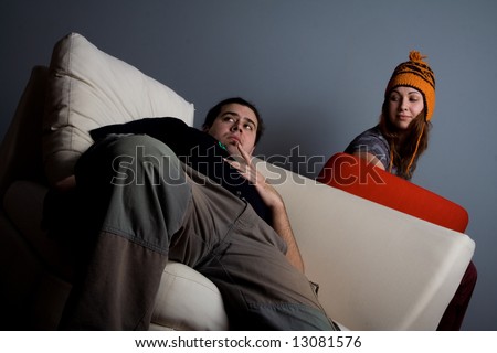 Woman and man sitting on couch, looking left, bored. Strong light and shadows