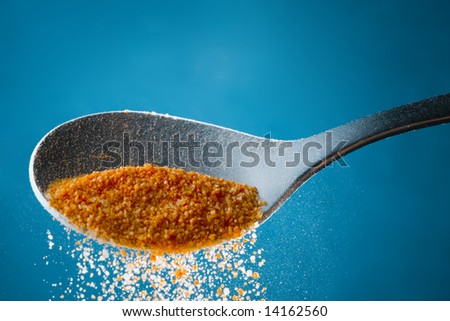 Metal spoon filled with food ingredient powder / grains over blue isolated background.