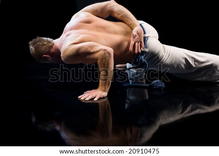 Young handsome man doing push-up  on one hand on black background
