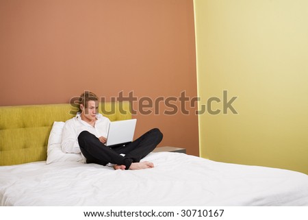 Young handsome man working on a laptop on big bed