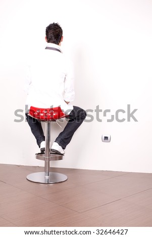 Young man back sitting in modern chair facing white wall. Very bright light