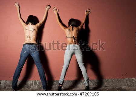 Two young women arrested, standing against the wall for searching