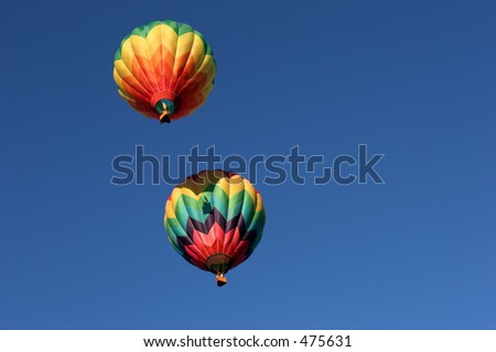 two colorful hot air balloons, top one casting its shadow of the basket as it fires its burners to climb