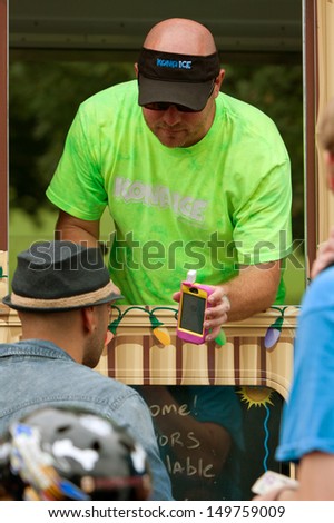 ATLANTA, GA - JULY 27:  A vendor uses his smart phone to confirm a credit card transaction with a customer at the Atlanta Ice Cream Festival in Piedmont Park, on July 27, 2013 in Atlanta.   .