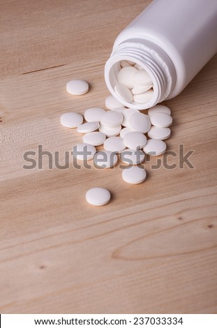 White pills spilled from a pill bottle on wooden table.