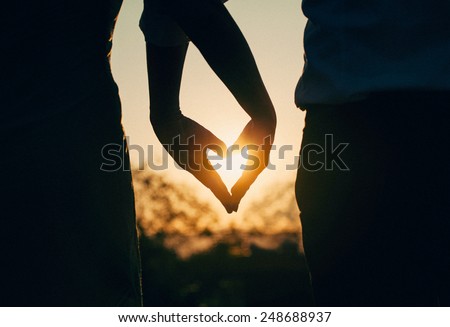 Silhouette of couple holding hands in heart shape with sunset in  the middle. Vintage, retro toned photo.