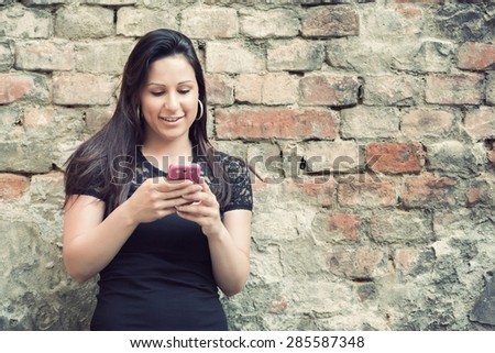 Beautiful young woman in black shirt and jeans reads message to mobile phone. Toned photo.