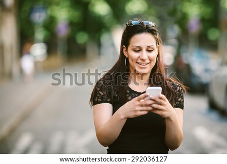 Smiling beautiful woman texting with her mobile phone. Toned photo, shallow depth of field.