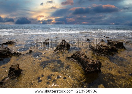 receding sea coastline and stone with water pits at sunset