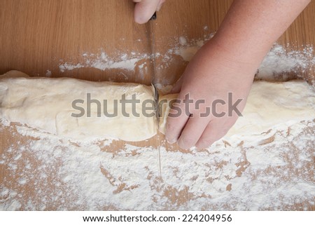 hand with a knife cut dough for rolls