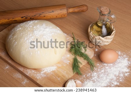 dough on a board with flour. olive oil, eggs, rolling pin, garlic and dill