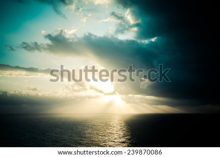 Dramatic sunset rays through a cloudy dark sky over the ocean. Tinted