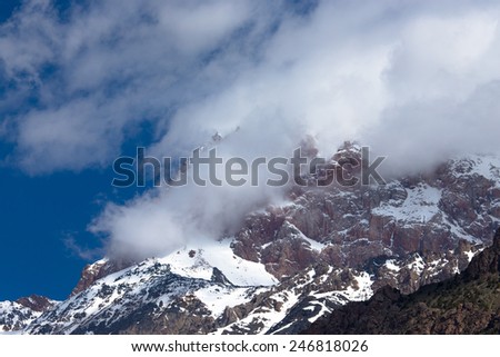 Clouds lie on the snow-covered tops of the rocks. Landscape.