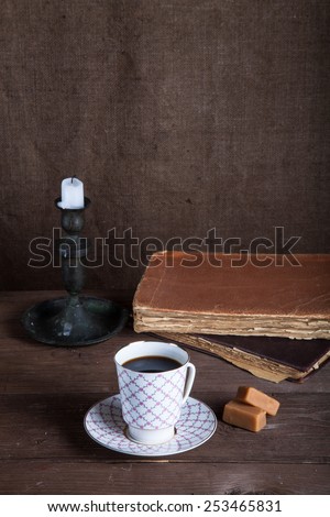 Stack of old books, cup of coffee, candy and candle on the old wooden table.