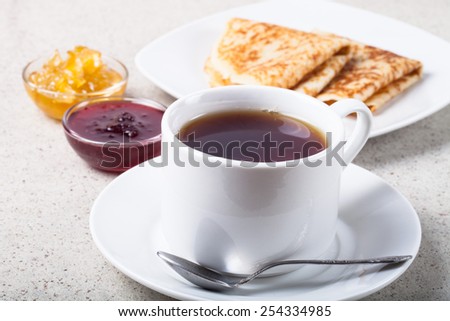 Cup of tea with two kinds of jam and russian pancakes - blini.
