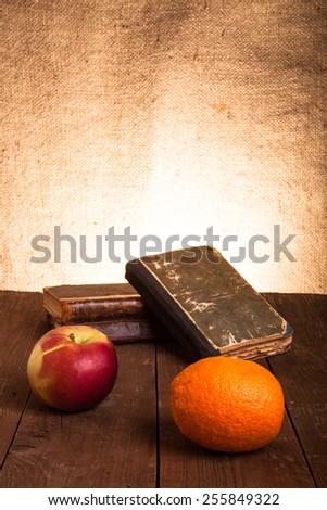 old books, apple and orange lying on an old wooden table.
