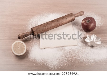 Dough, rolling pin, forms for baking, apple, half of lemon and flour sprinkled on a light wooden table. Toned.