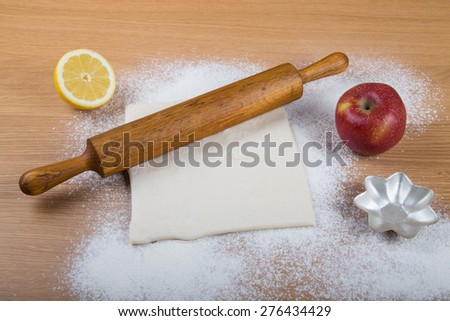 Dough, rolling pin, forms for baking, apple, half of lemon and flour sprinkled on a light wooden table.