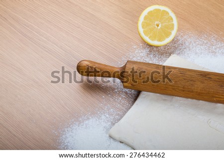 Dough, rolling pin, half of lemon and flour sprinkled on a light wooden table.