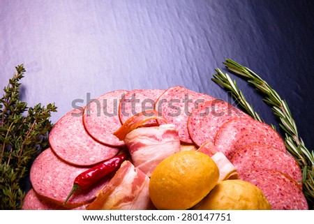 plate of sliced sausage, peppers, herbs and French bread rolls on a dark background. Tinted