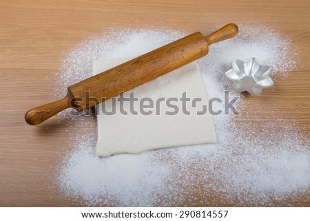 Rolling pin, dough and baking form on a light wooden table with flour.