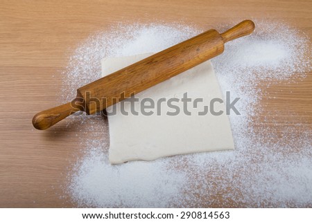 Rolling pin, dough and baking form on a light wooden table with flour.