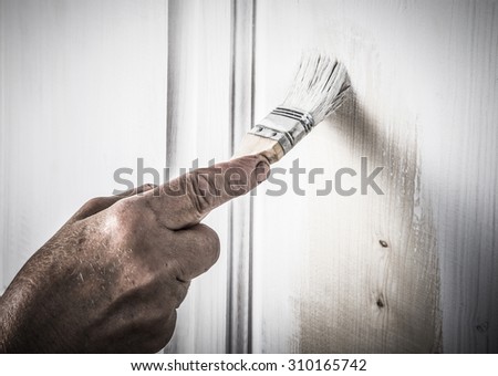 Hand of an elderly woman with a paint brush with white paint door. Selected focus